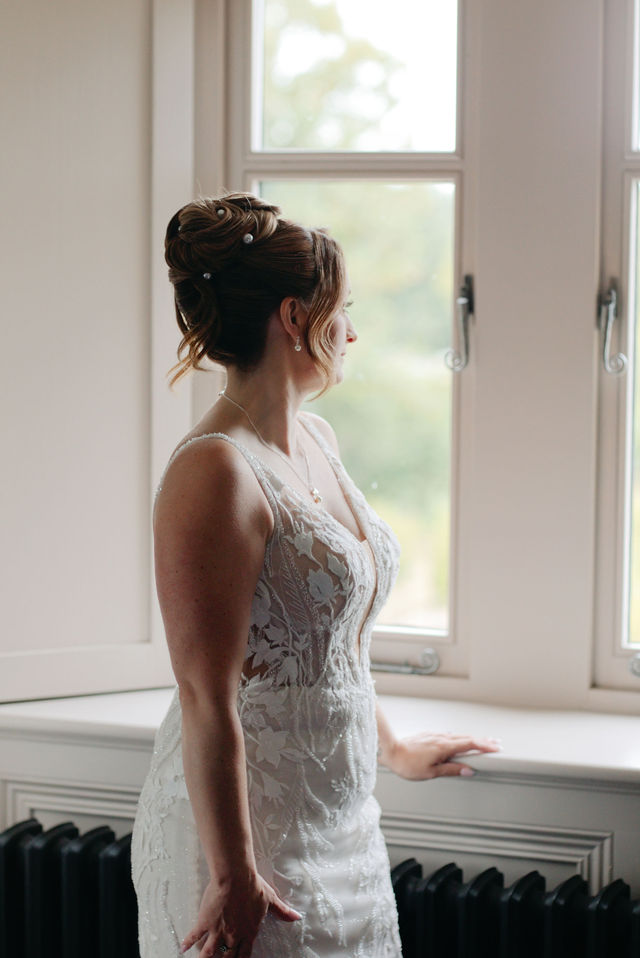 Katie in her wedding dress beside a sunlit window