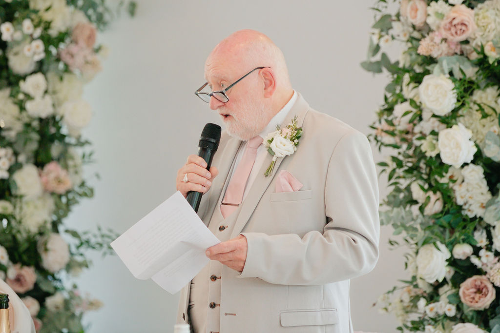 A wedding speech beside the pink and white floral arrangements