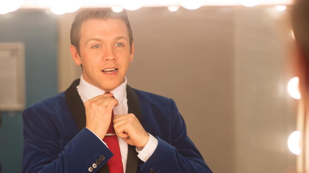 A performer adjusting his tie in a dressing-room mirror